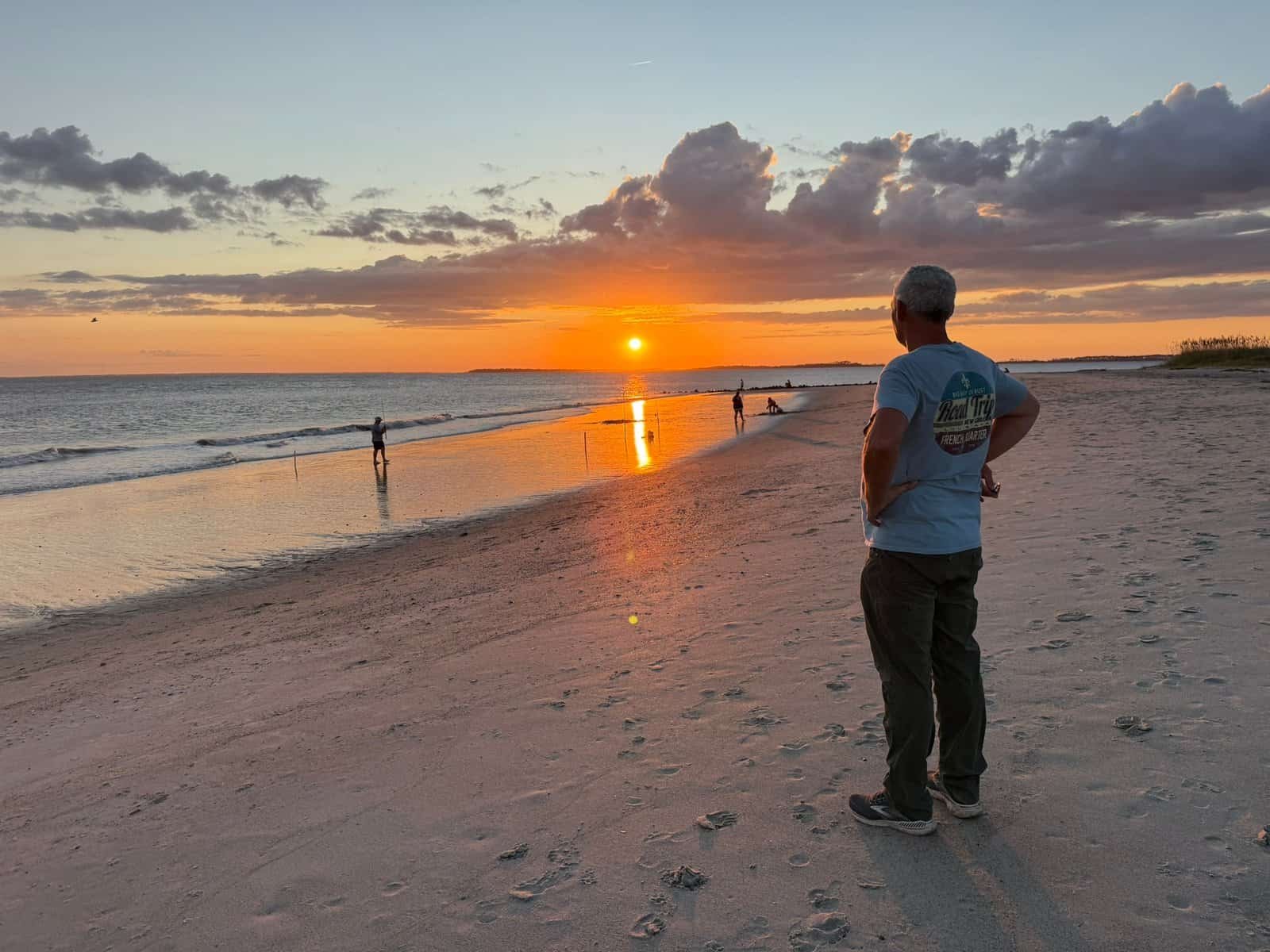 standing on the beach during sunset, enjoying the view of the ocean and colorful sky, capturing a peaceful moment in nature.